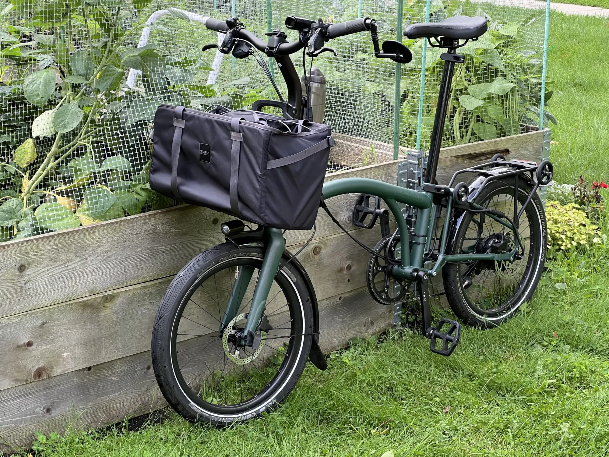 A three quarter front view of a bike. There's a large bag hanging on the front. The bike is leaning against a raised vegatable garden bed..